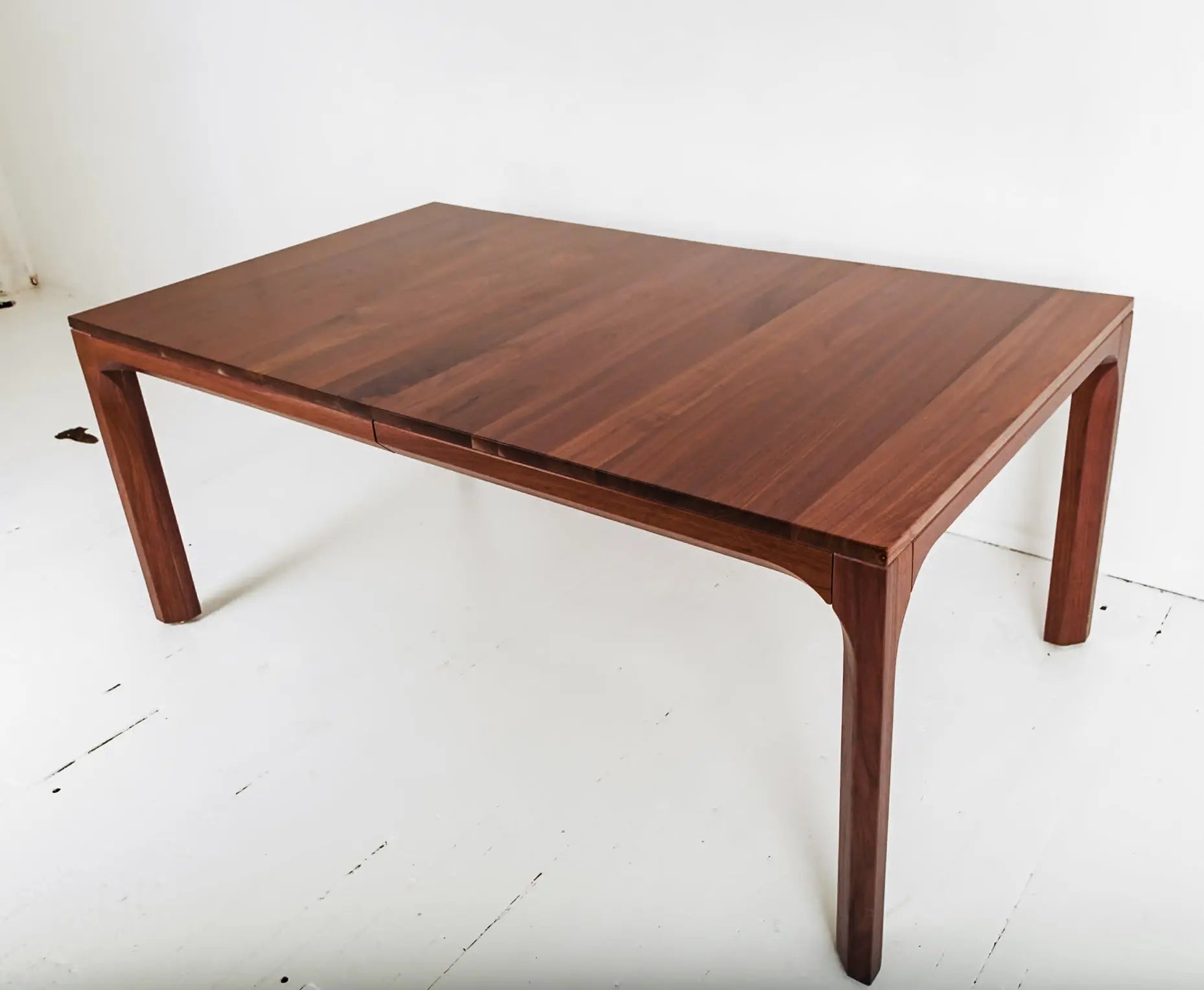 Solid walnut dining table with vibrant orange chairs in a minimalist space
